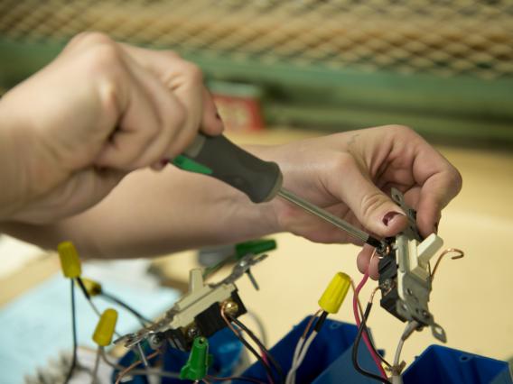 A student's hand wiring a light switch. 